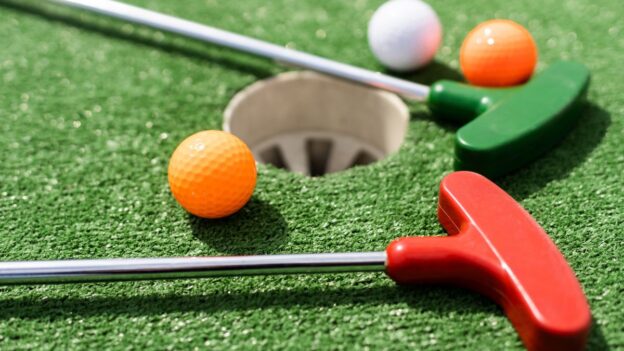 Mini golf putters and colorful balls beside a putting green hole
