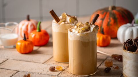 A perfectly spiced pumpkin latte topped with velvety cold foam and a sprinkle of cinnamon, served against a backdrop of warm fall décor.