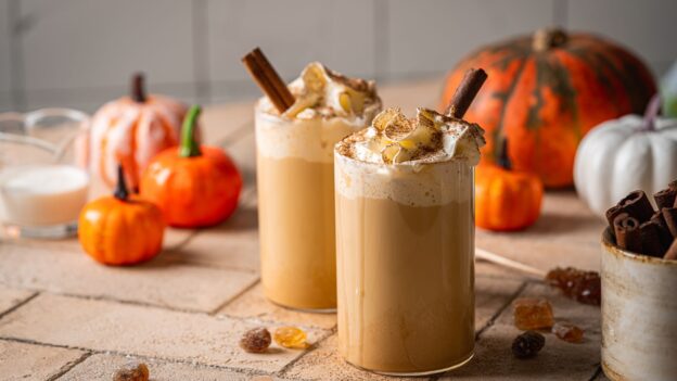 A perfectly spiced pumpkin latte topped with velvety cold foam and a sprinkle of cinnamon, served against a backdrop of warm fall décor.