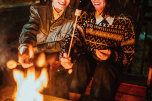 two people sitting by a fire pit roasting marshmallows
