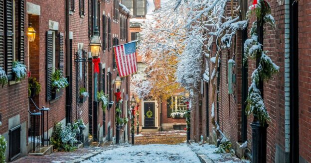Snow-covered Acorn Street in Beacon Hill with brick rowhouses and holiday greenery in winter.