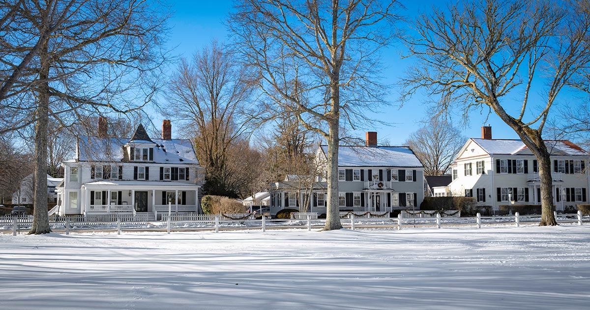 Historic New England homes along a snowy village green on a clear winter day in Massachusetts.