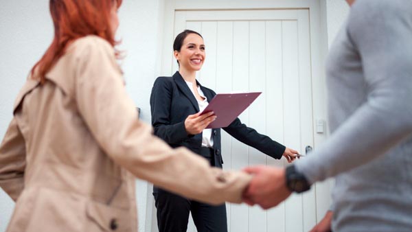 Real estate agent welcoming clients at the front door for a home showing
