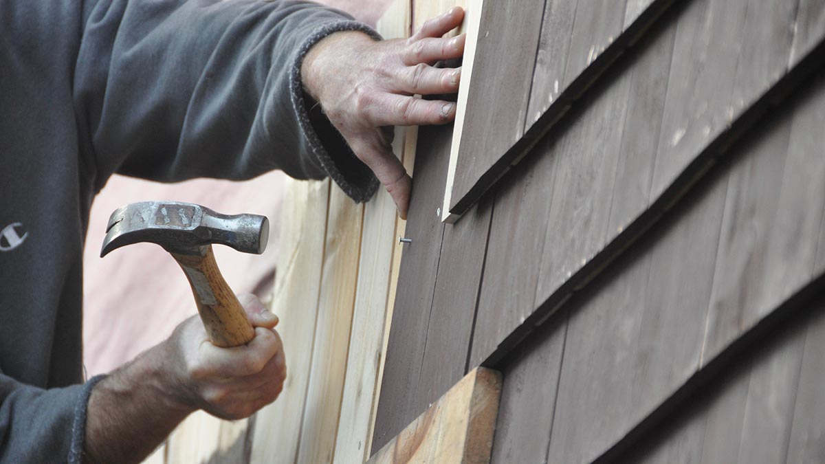 Professional repairing wood-shingle siding on a coastal home