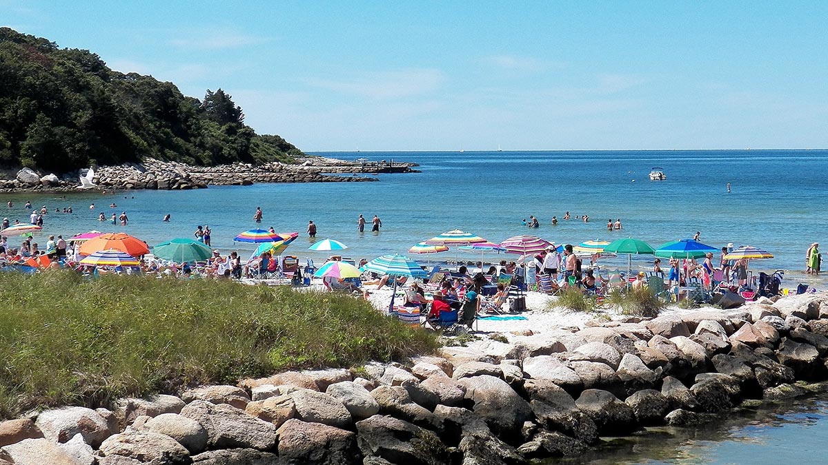 Beachgoers swimming and relaxing under colorful umbrellas at Old Silver Beach in Falmouth
