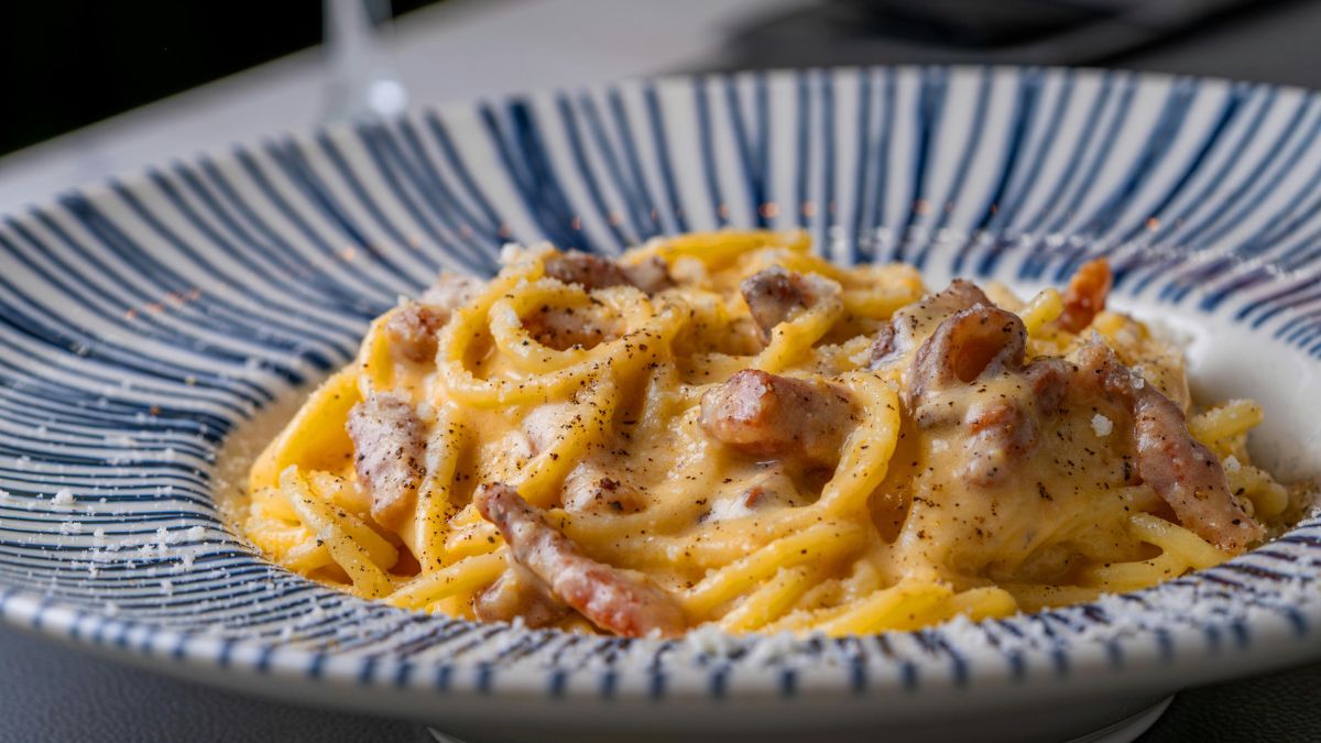 Creamy pasta topped with cheese and pancetta on a blue and white plate