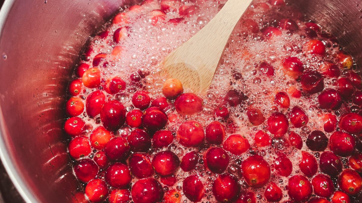 Cranberries simmering in a saucepan with a wooden spoon