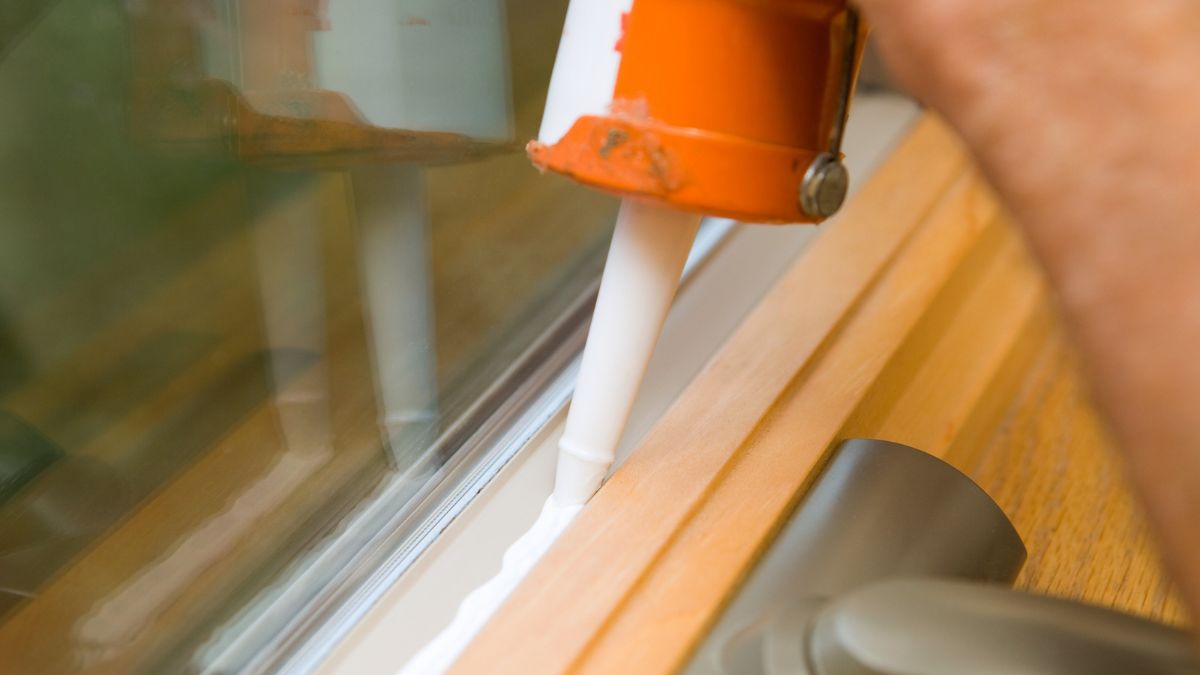 Applying caulk along a window frame to seal drafts before winter