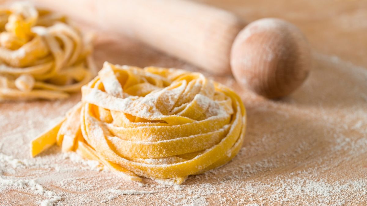 Nest of fresh homemade pasta on a floured work surface with a wooden rolling pin